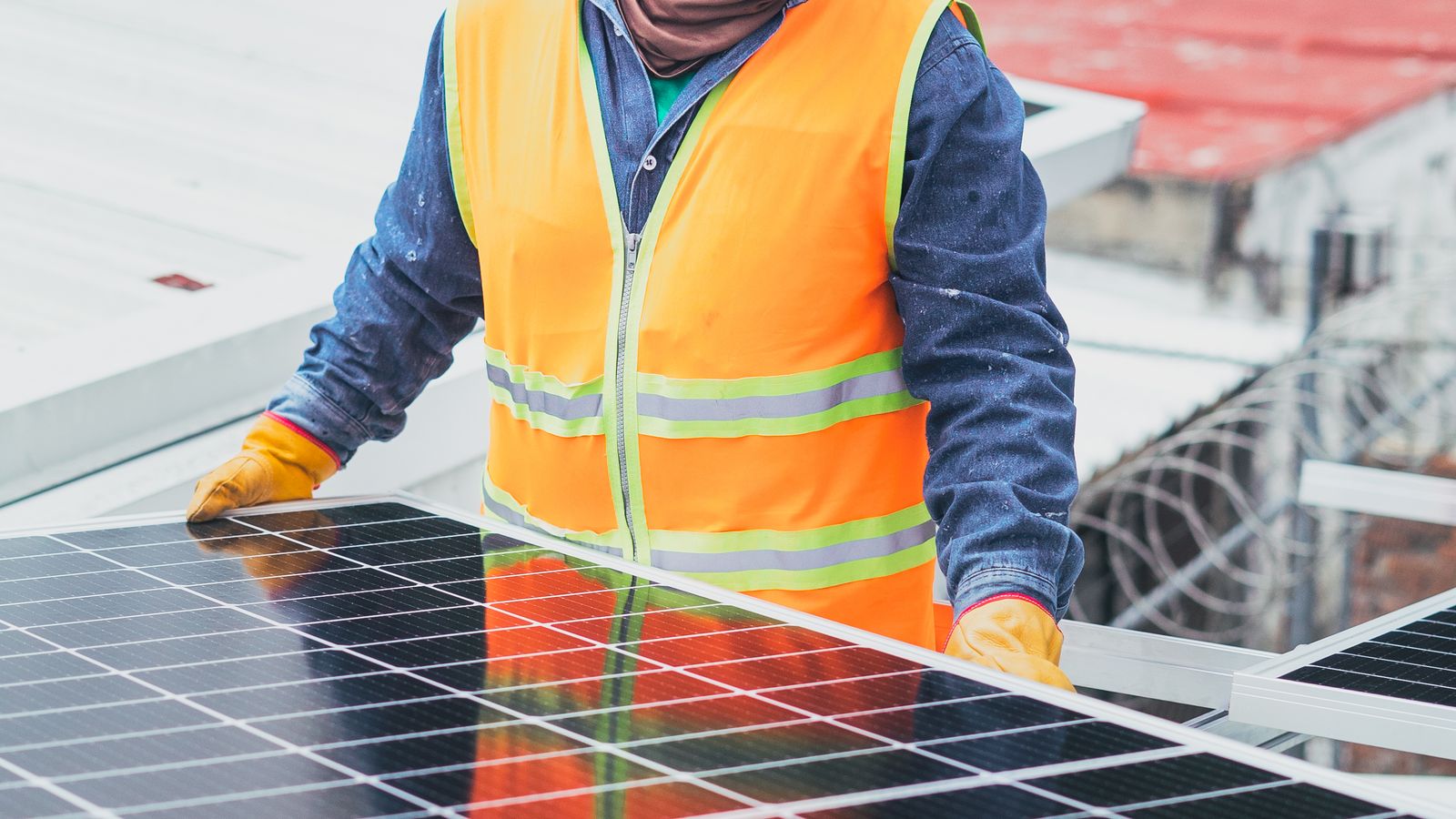Technicien en gilet de sécurité contrôlant un panneau photovoltaïque en toiture
